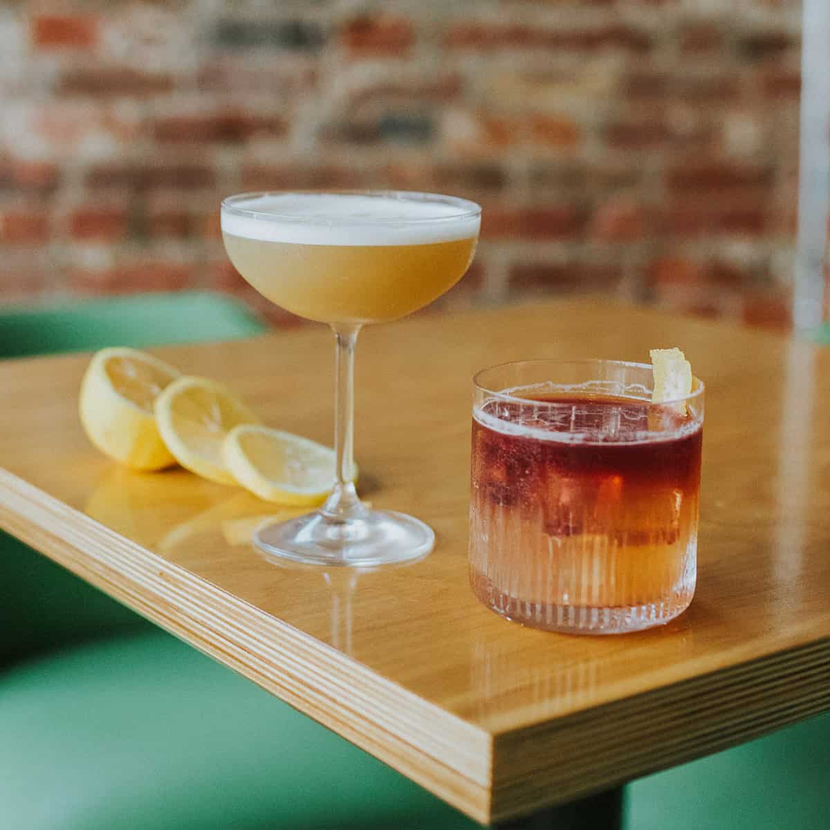 a classic whiskey sour and a new york sour on a table with slices of lemon